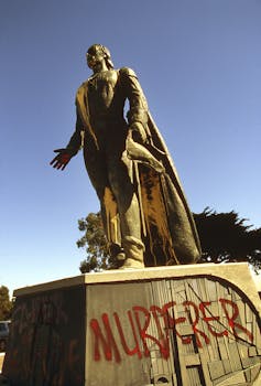 Uma estátua de Cristóvão Colombo é vandalizada com a palavra 'assassino' pintada em vermelho.