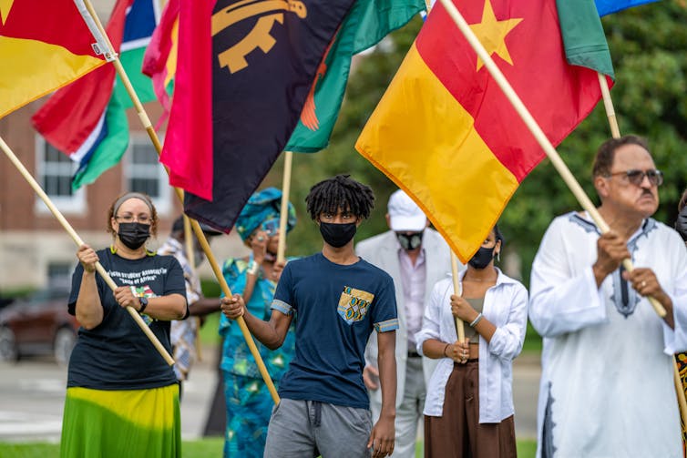 A group of people march, wearing masks and holding flags.