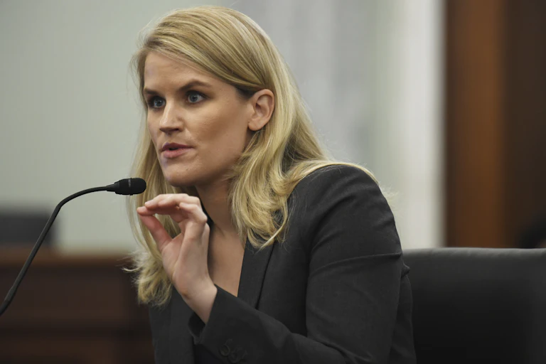 A woman speaks into a microphone while gesturing with her left hand
