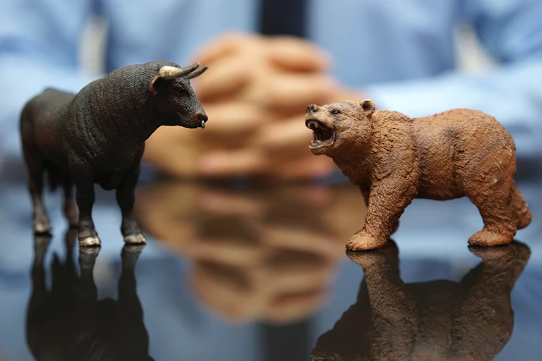 A model bull and bear on a table in front of a man in a shirt and tie
