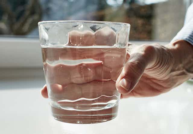 A woman holds out a glass of water with a wind in the background