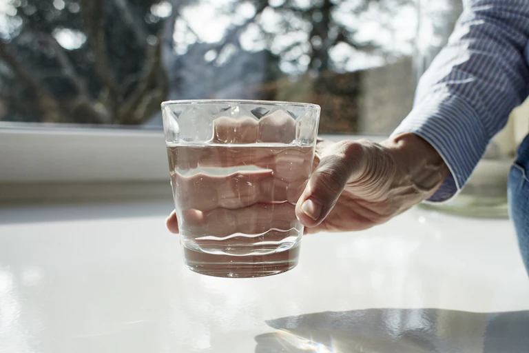 A woman holds out a glass of water with a wind in the background