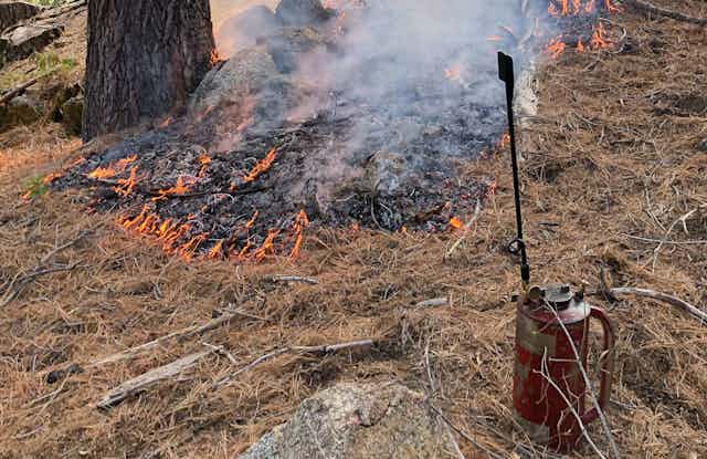 A small fire and a drip torch used by firefighters to set controlled burns.