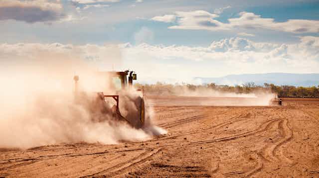 tractor ploughs dusty field