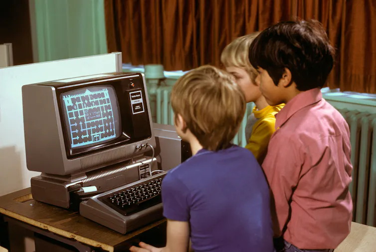 Three children sit in front of an early Radio Shack TRS80 computer