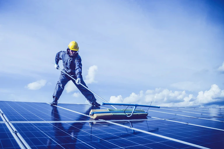A person cleans a solar panel on a roof
