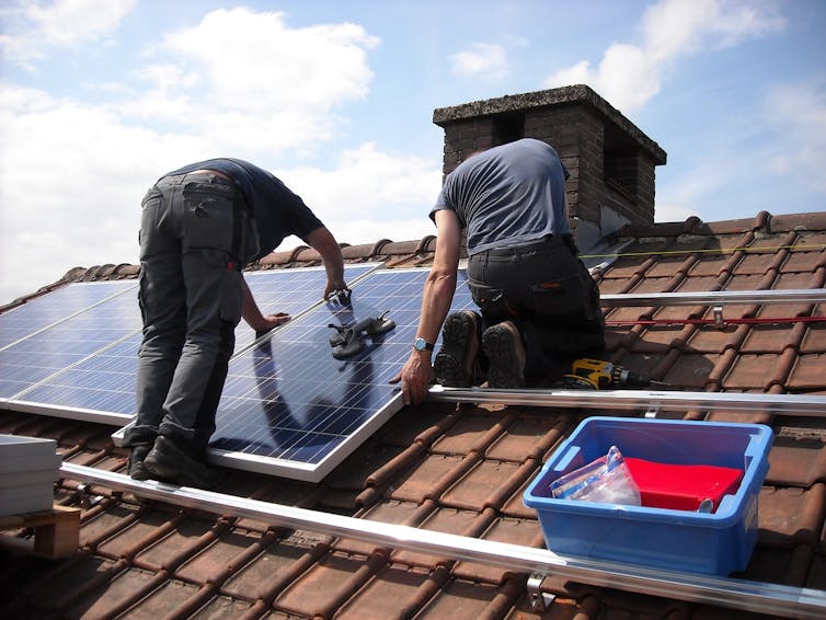 Two people work on a solar panel on a roof