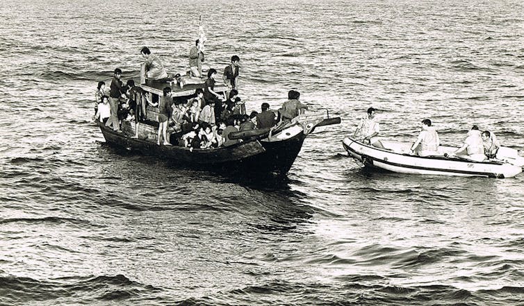 People are seen crowded onto a small boat in a black and white photo.