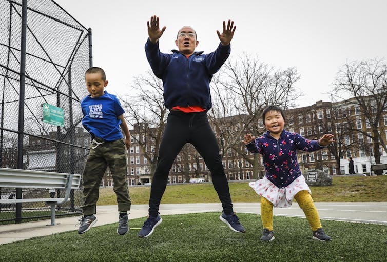 A father, son and young daughter jump while exercising outdoors together