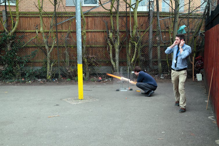 A teacher demonstrates a rocket launch in a science class held outdoors