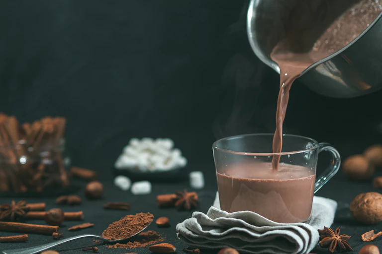 Hot chocolate is poured into a clear glass mug