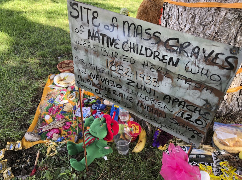 A sign saying "site of mass graves of Native children who were buried here from 1882 - 1933,"  in Albuquerque, New Mexico.