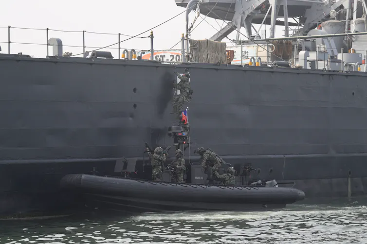 Military personnel climb from a rubber dinghy on to a ship.