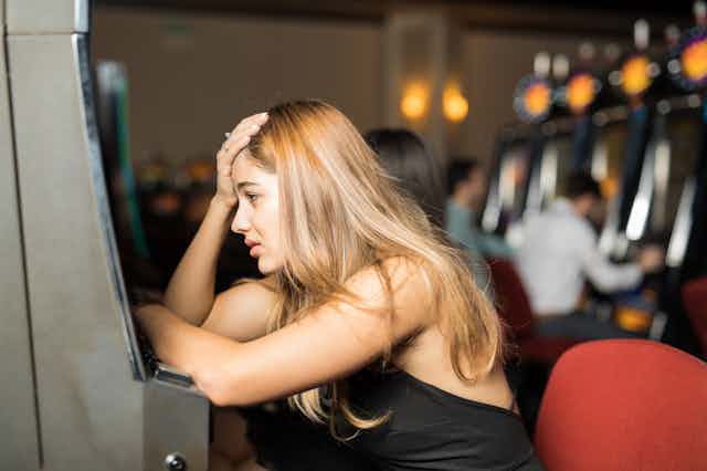 Mujer desafortunada que se ve triste y estresada después de perder todo su dinero en una máquina tragaperras en un casino
