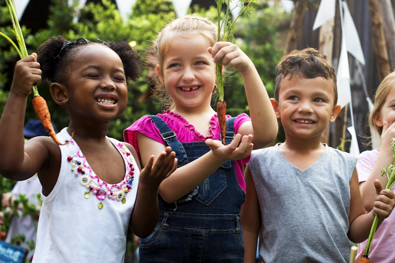 Children hold up carrots outdoors.
