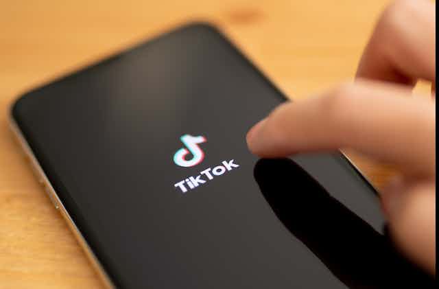 Hand touching a mobile phone screen with TikTok logo