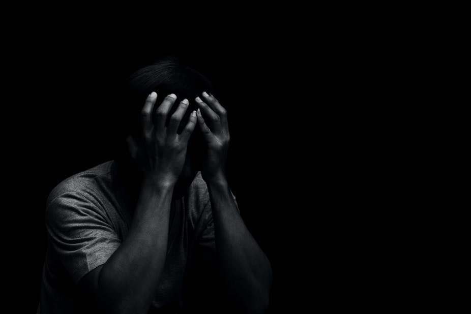 A black background picture of a man putting his hands over his face