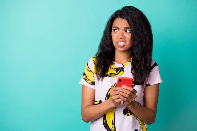 A woman looks disgusted while holding her phone.