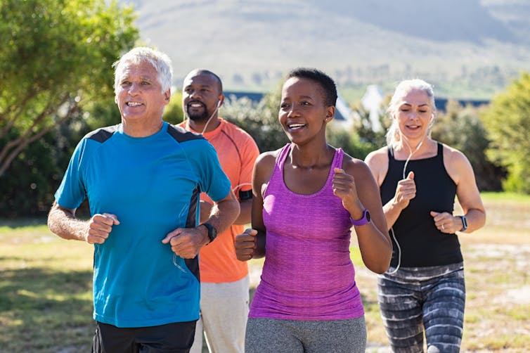 A group of four adults running together outdoors.