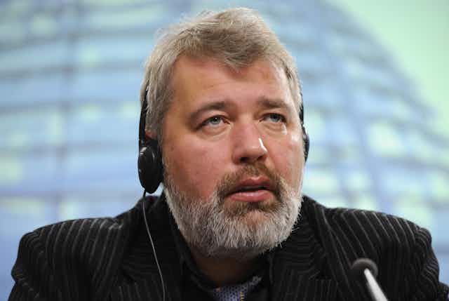 Shoulders-up photo of Dmitry Muratov wearing headphones and speaking into a microphone