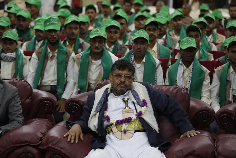 Houthi leader Mohammed Ali al-Houthi sits with fighters wearing the green uniform and caps of the Iran-based Houthi rebels.