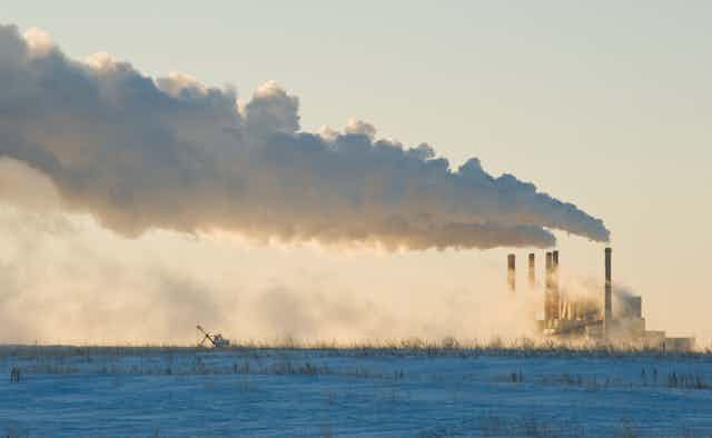 A power plant with five chimneys spewing smoke on a frozen field.