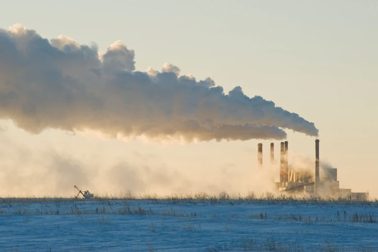 A power plant with five chimneys spewing smoke on a frozen field.