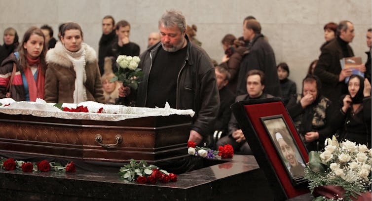 Dmitry Muratov brings flowers to an open coffin with crowd behind