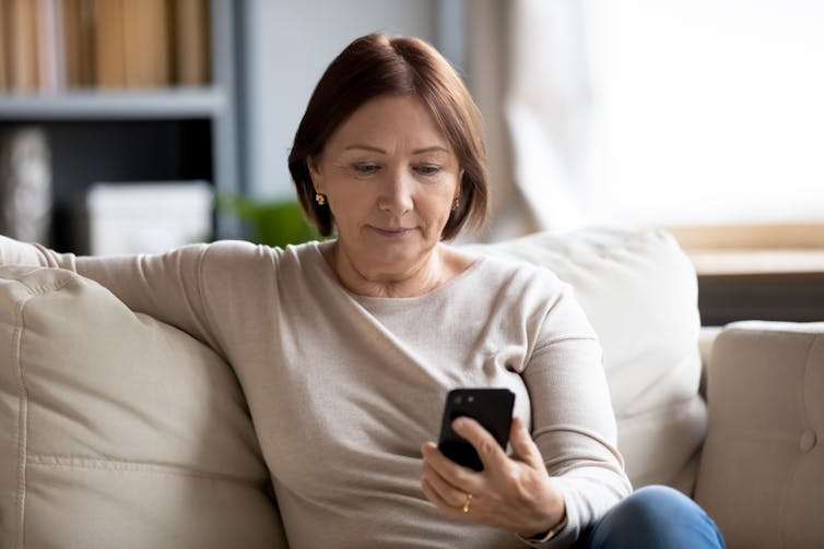 A woman sits on the couch looking at her smartphone.