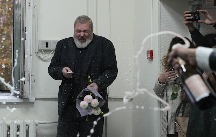 Dmitry Muratov cowers from streams of champagne fly out of bottles held by well-wishers.