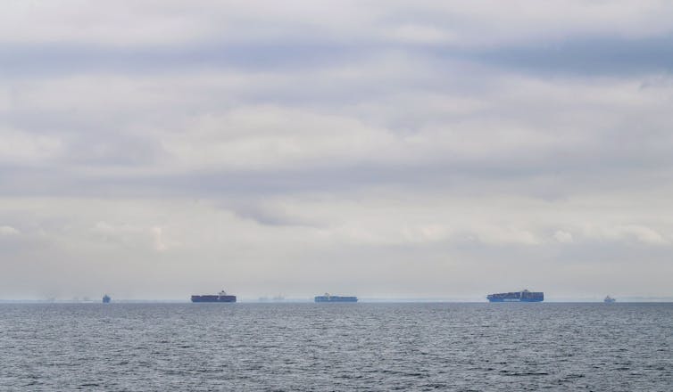 Cargo ships filled with containers idle in waters off of California on a cloudy day as they await entry to the Port of Los Angeles or Port of Long Beach