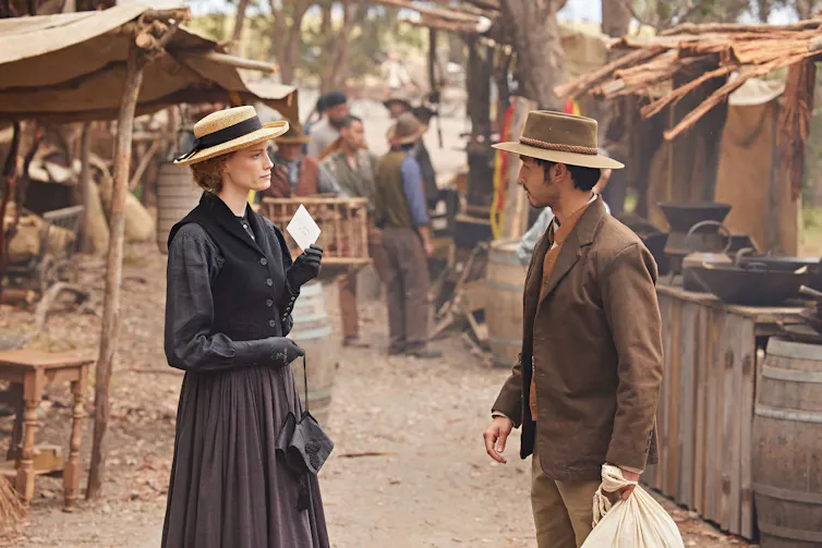 Production image: a white woman and an Asian man talk.