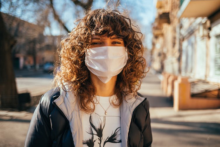 Young woman in mask, outside in the sun, smiling.