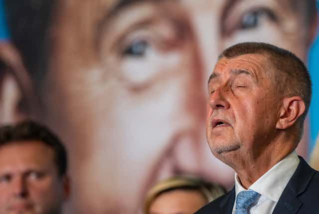 Czech prime minister Andrej Babis closes his eyes while talking to the press in front of a large picture of himself.
