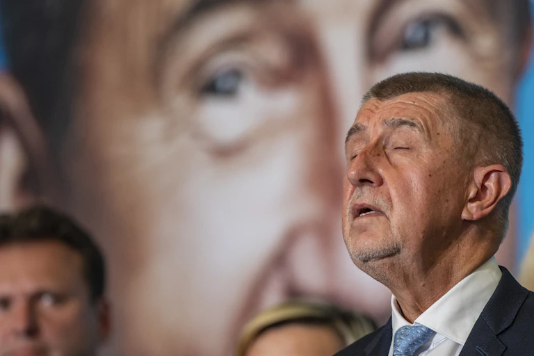 Czech prime minister Andrej Babis closes his eyes while talking to the press in front of a large picture of himself.