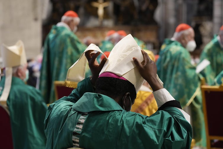 A Bishop in green robes adjusts his hat at a mass in St. Peter's Basilica in the Vatican.