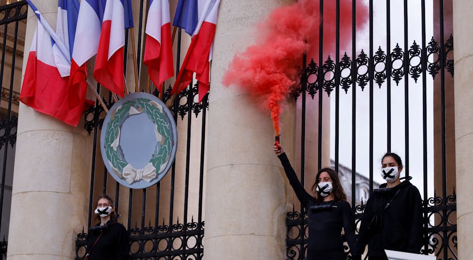 Des militants de l'organisation Extinction Rebellion (XR) tiennent une fusée de détresse alors qu'ils se tiennent enchaînés aux grilles de l'Assemblée nationale (Parlement français) à Paris, le 4 mai 2021, lors d'une manifestation pour protester contre le projet de loi sur le climat.