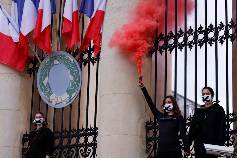 Des militants de l'organisation Extinction Rebellion (XR) tiennent une fusée de détresse alors qu'ils se tiennent enchaînés aux grilles de l'Assemblée nationale (Parlement français) à Paris, le 4 mai 2021, lors d'une manifestation pour protester contre le projet de loi sur le climat.