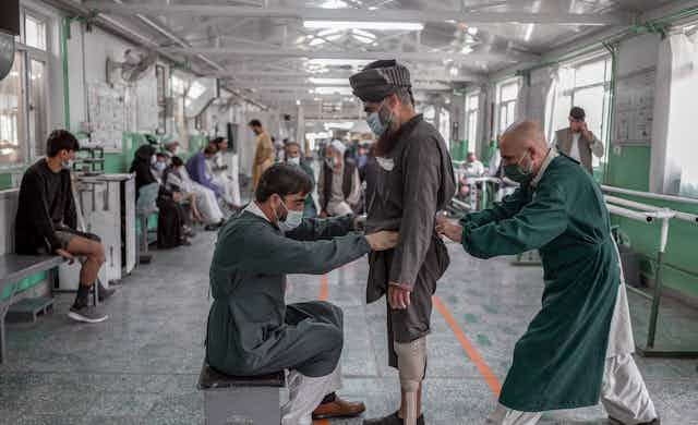 Two men assist an Afghan fitted with a prosthetic leg. 