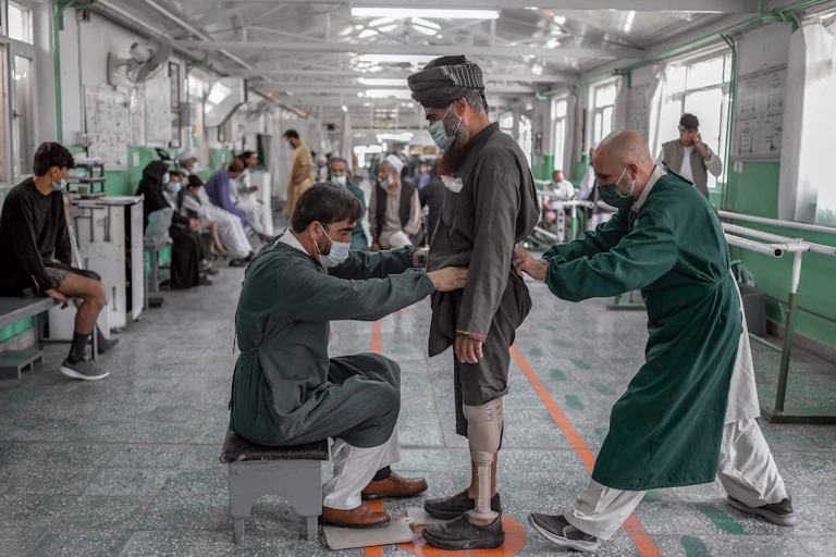 Two men assist an Afghan fitted with a prosthetic leg.
