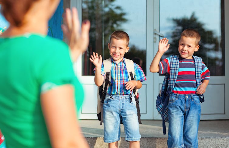 Two young boys wave to mother at school entrance