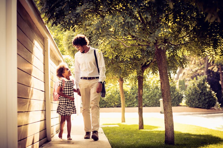 Father and daughter laugh together as they walk to school.