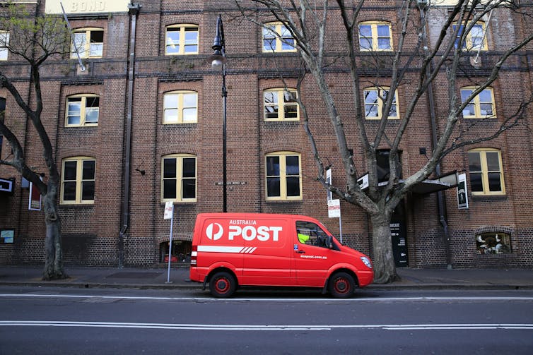 An Australia Post van waits outside a building.