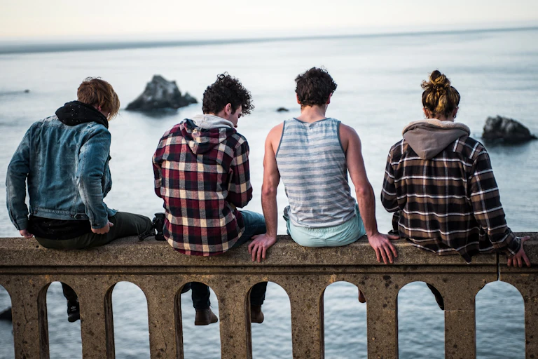 Un groupe de quatre jeunes, assis sur un muret et vus de dos, regarde l'océan.