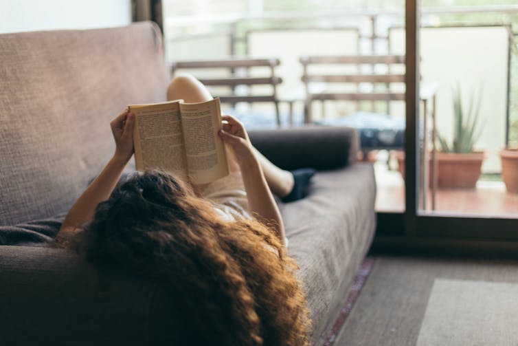 A woman lying on a sofa reading a book