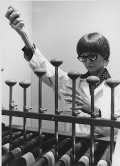 Black and white photo of a woman using a large pipette to measure out a chemical liquid.