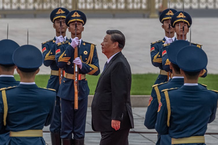 Chinese president Xi Jinping walks past soldiers in dress uniform standing at full attention.