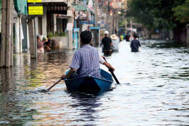Man paddles canoe down flooded street in Asian city