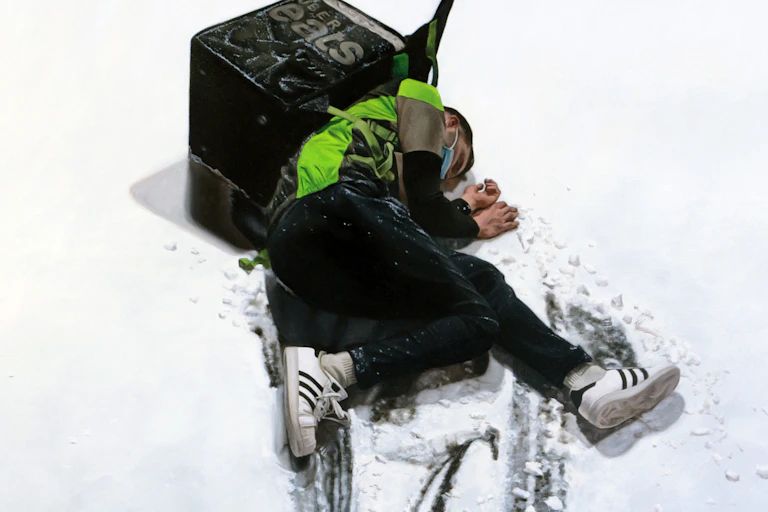 Un livreur Uber Eats à terre, dans la neige. Il est inconscient et semble blessé.