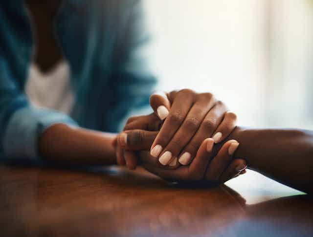 Close-up shot of two people holding hands in comfort.